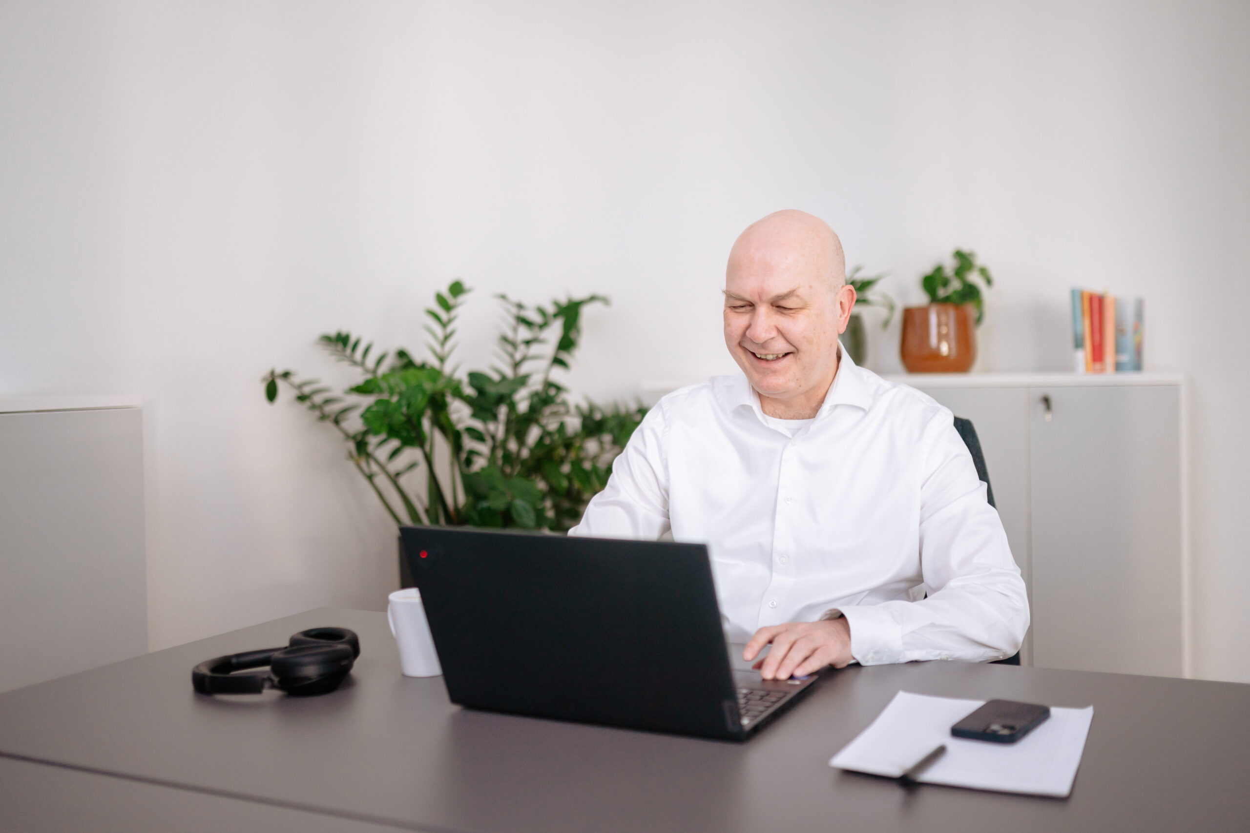 Mann arbeitet konzentriert am Laptop in hellem Büro mit Pflanzen und moderiert den Prozess, macht Notizen für eine Anforderungsanalyse