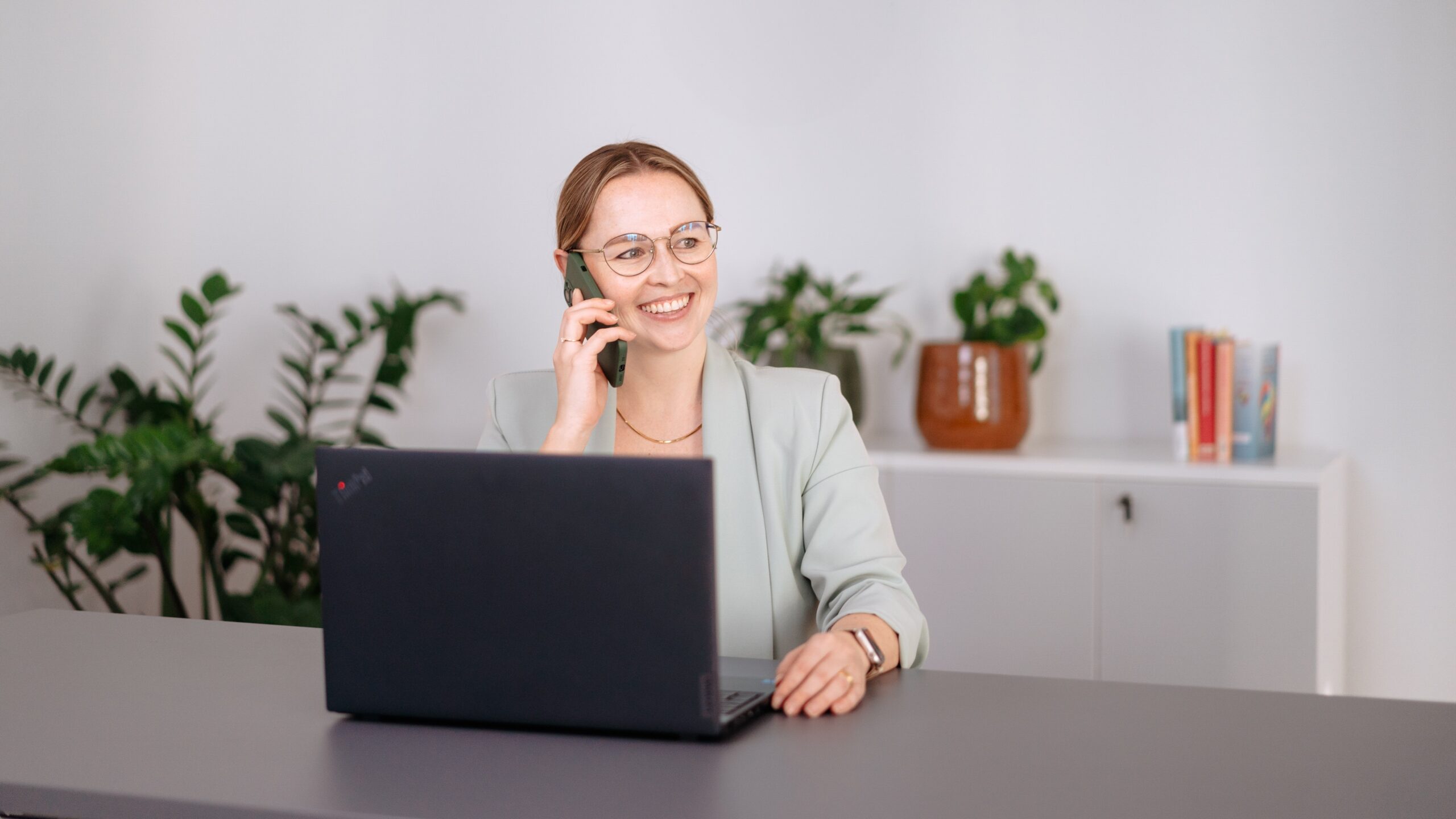 Kontakt Frau telefoniert freundlich am Laptop in modernem Büro mit Pflanzen für Personal- und Organisationsberatung
