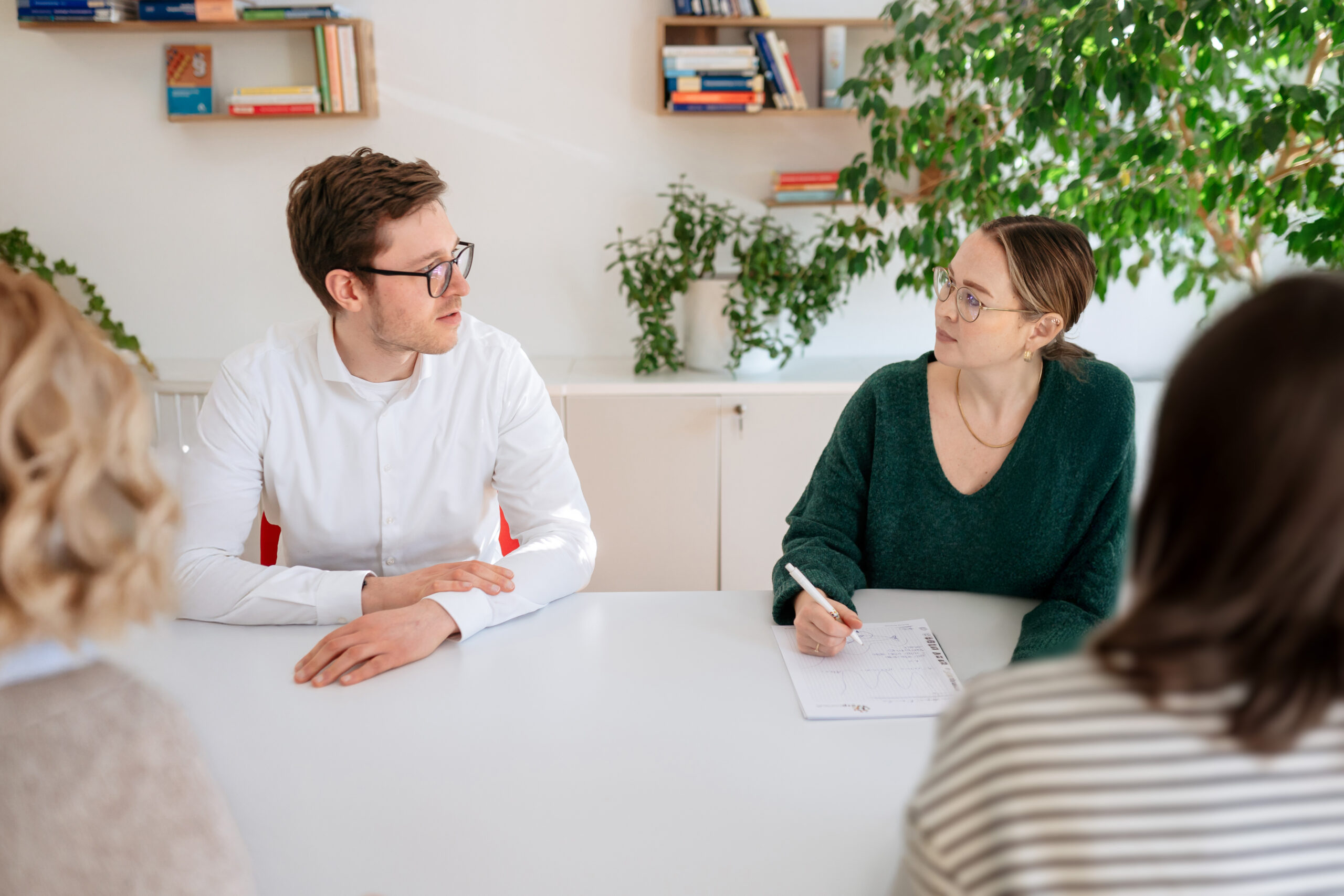 Mehrwert Epilog Entwicklungsgespräch Vier Personen diskutieren angeregt in heller moderner Büroumgebung mit Pflanzen im Rahmen nächste Schritte zur Karriereentwicklung
