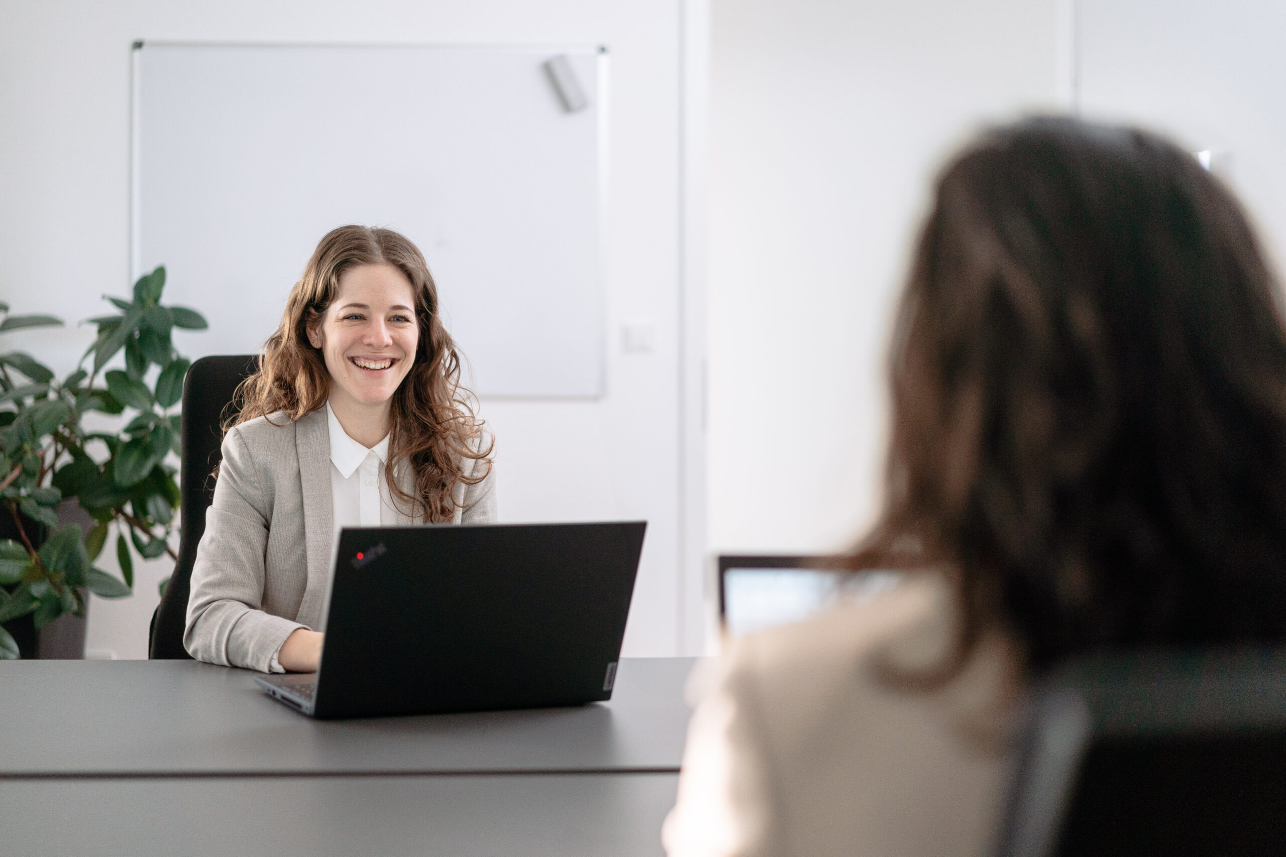Frau im Büro, lächelnd, im Gespräch, Laptop auf dem Tisch, professionelle Beratungssituation über beruflicher Erfolgsfaktoren, helle und freundliche Atmosphäre