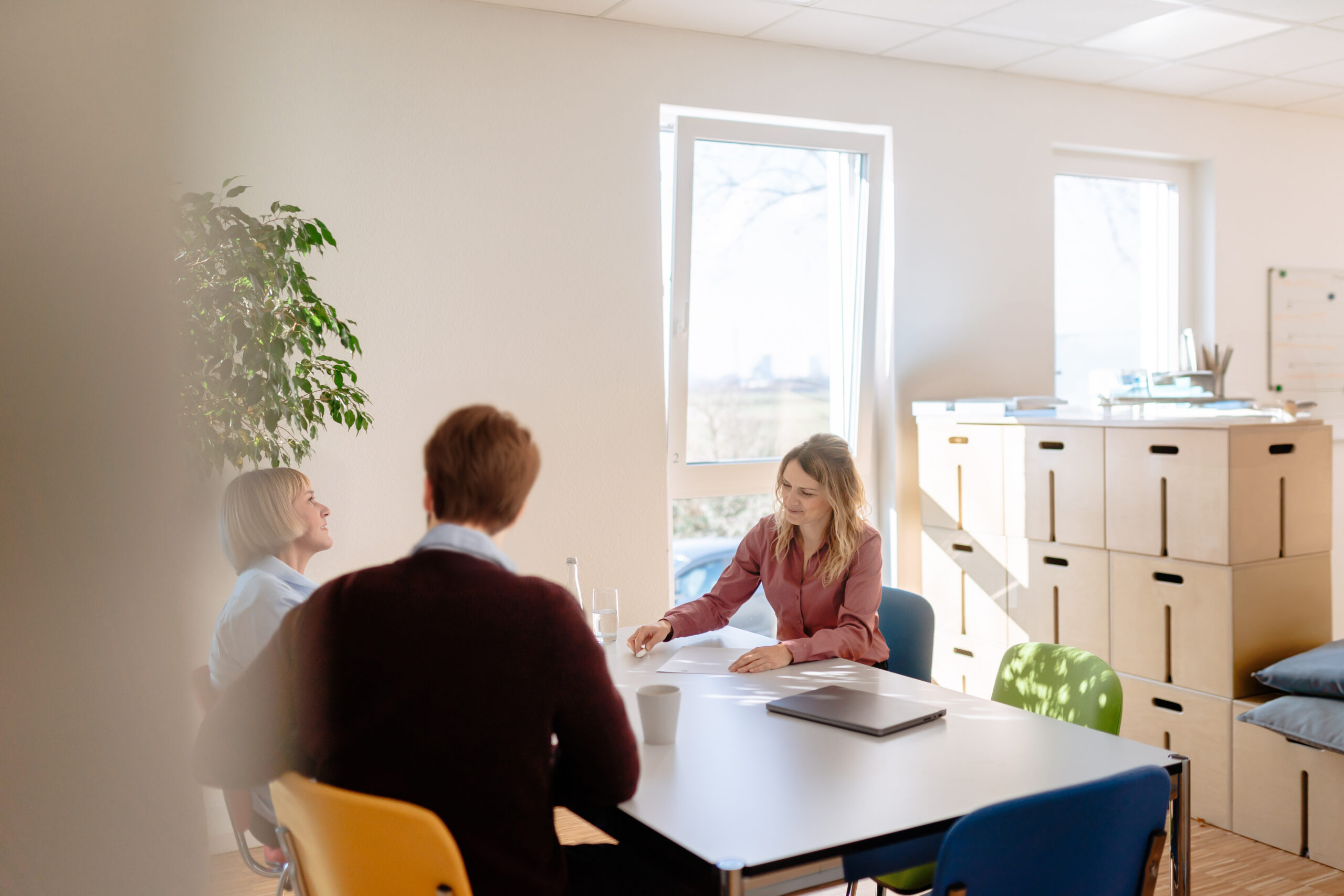 Überblick Kompetenzmanagement Drei Personen sitzen an einem Tisch im Gespräch, helle Umgebung, Unterlagen und Laptop vor ihnen, erarbeiten von Kompetenzen für eine Organisation