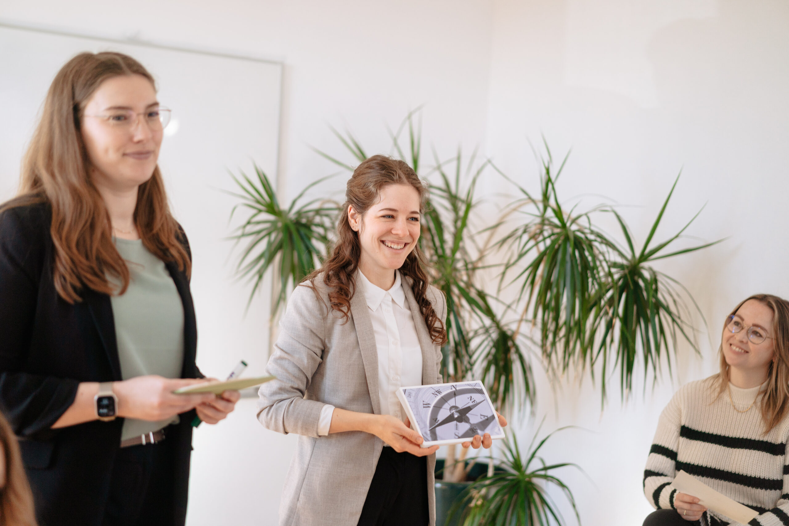 Drei Personen in freundlicher Runde, eine Frau präsentiert lächelnd eine Kompassgrafik, offene Gesprächsatmosphäre, Diskussion der Unternehmenskultur