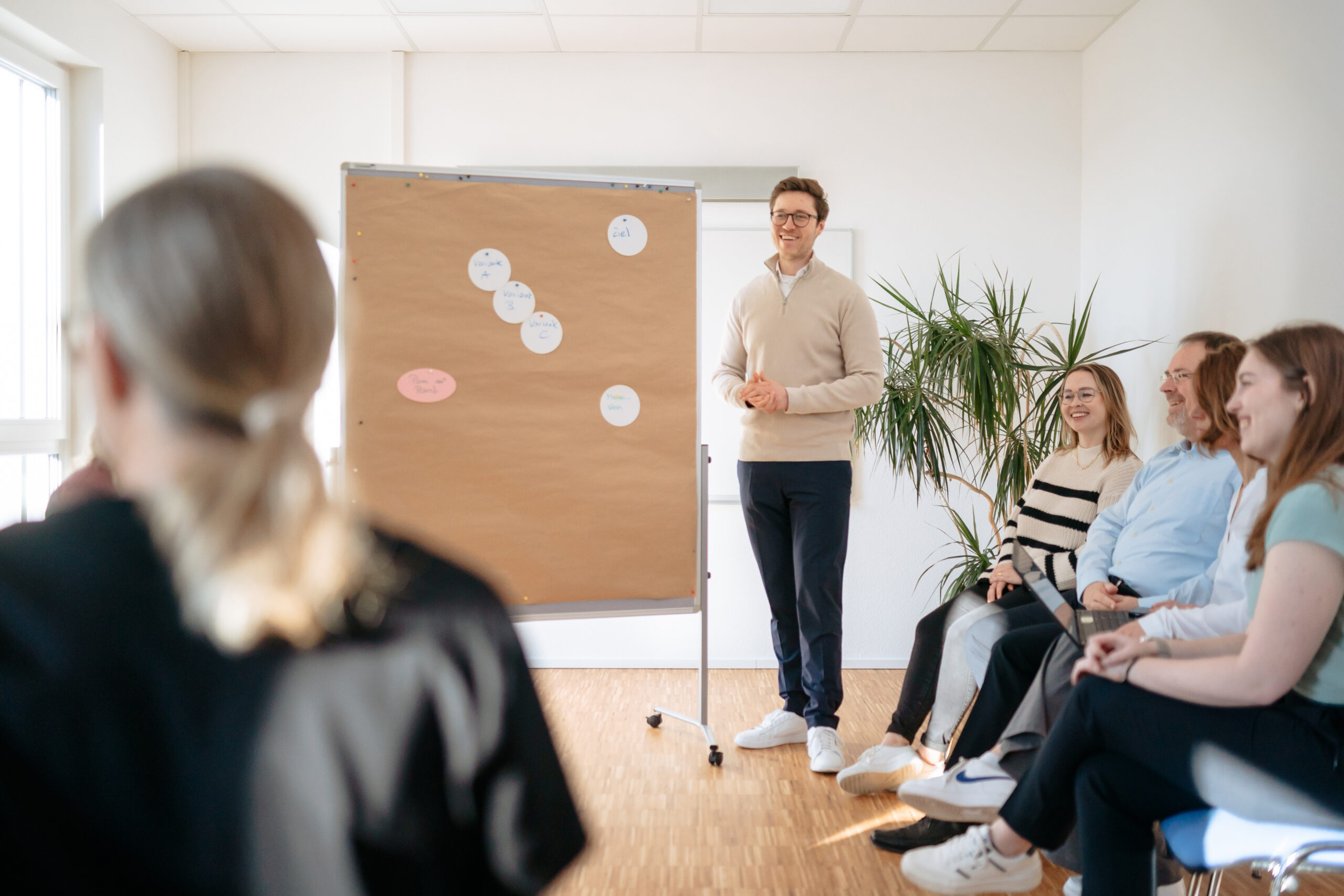 Überblick Teamentwicklung Moderator steht vor einer Gruppe von Menschen, offene, freundliche Atmosphäre, zugewandte Diskussion über die Entwicklung des Teams