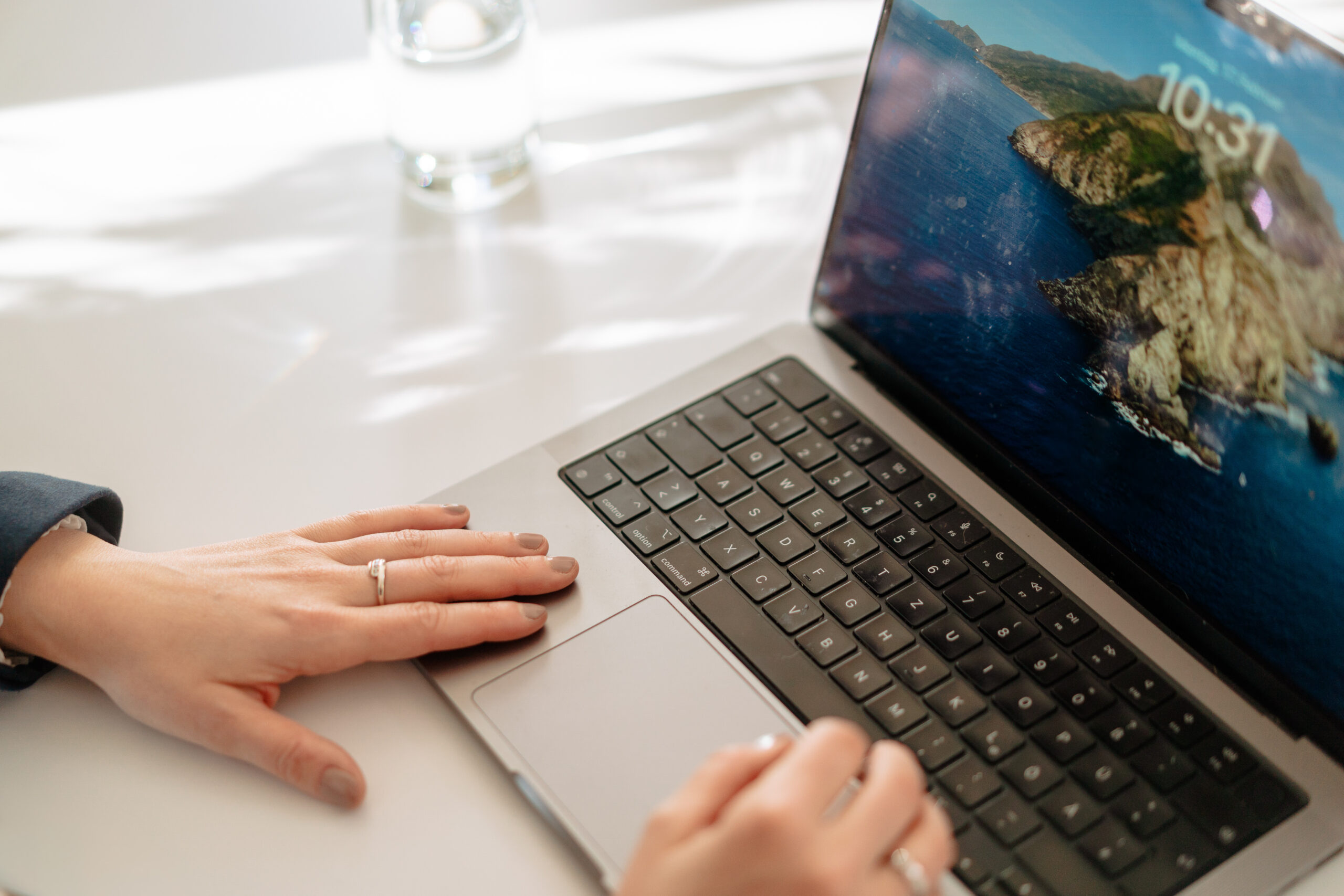 Nahaufnahme einer Person, die an einem Laptop arbeitet. Die Hände liegen an Tastatur und Touchpad, auf dem Bildschirm ist eine Landschaftsaufnahme zu sehen.