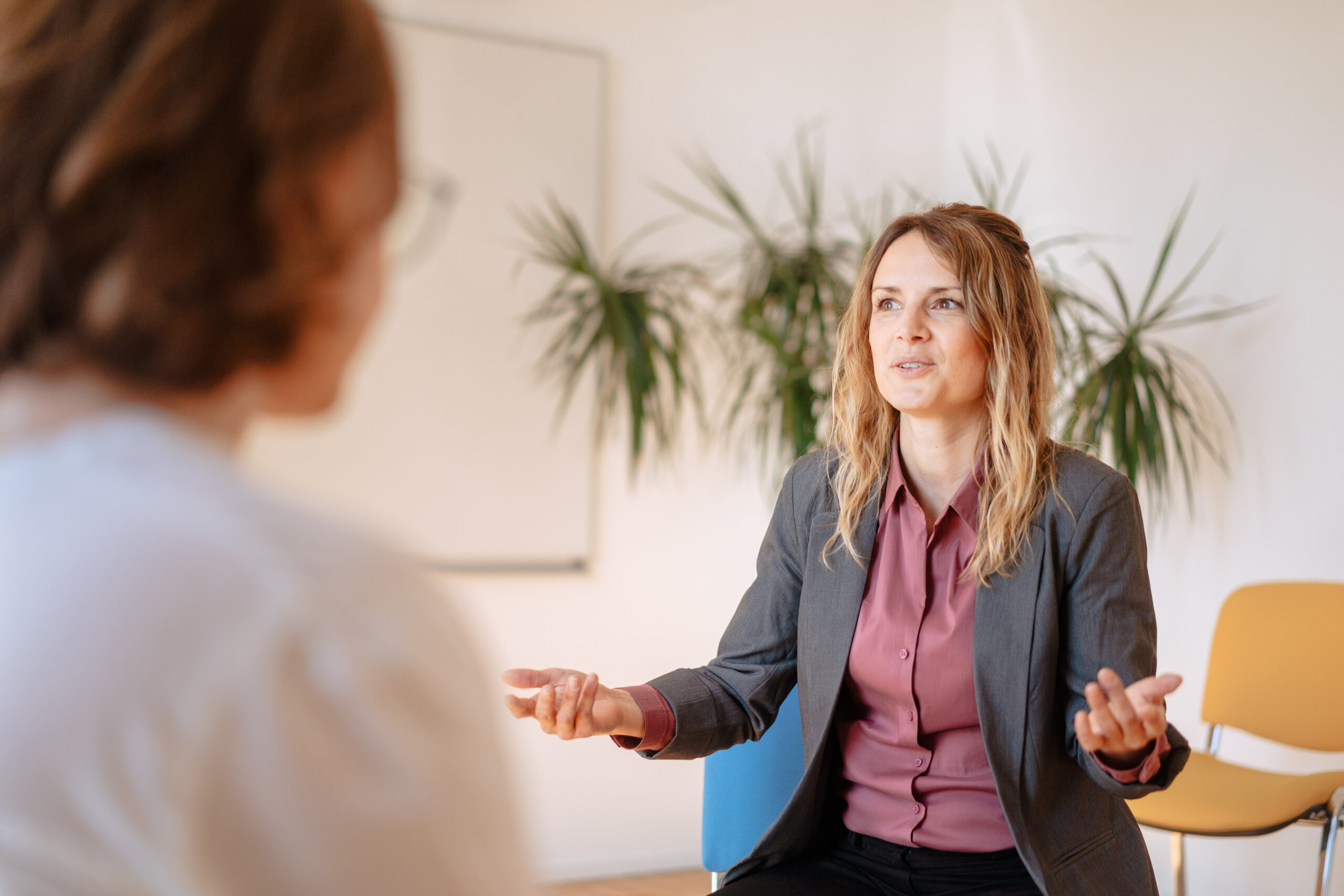 Unser Ansatz Coaching Coach sitzt mit offener Haltung ihrer Klientin gegenüber, Pflanze steht im Hintergrund, helle, moderne Büroräume