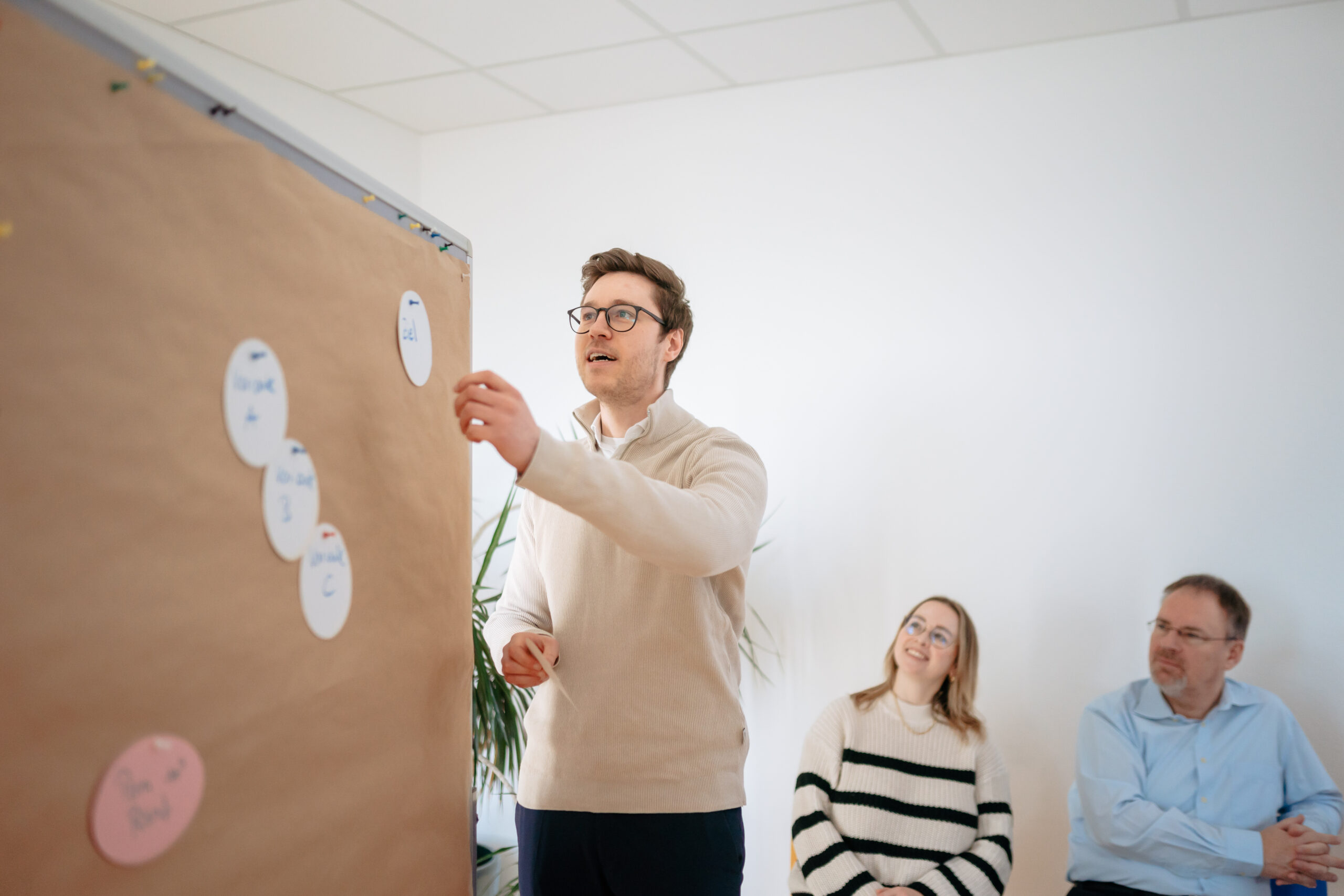 Ansatz Inhouse-Entwicklungsprogramme Ein Trainer steht vor einer Gruppe von Menschen, die ihnen zuhört, moderne Büroräume, helle Atmosphäre, umfassende Bearbeitung von Themen, interaktive Ausgestaltung, Vernetzung