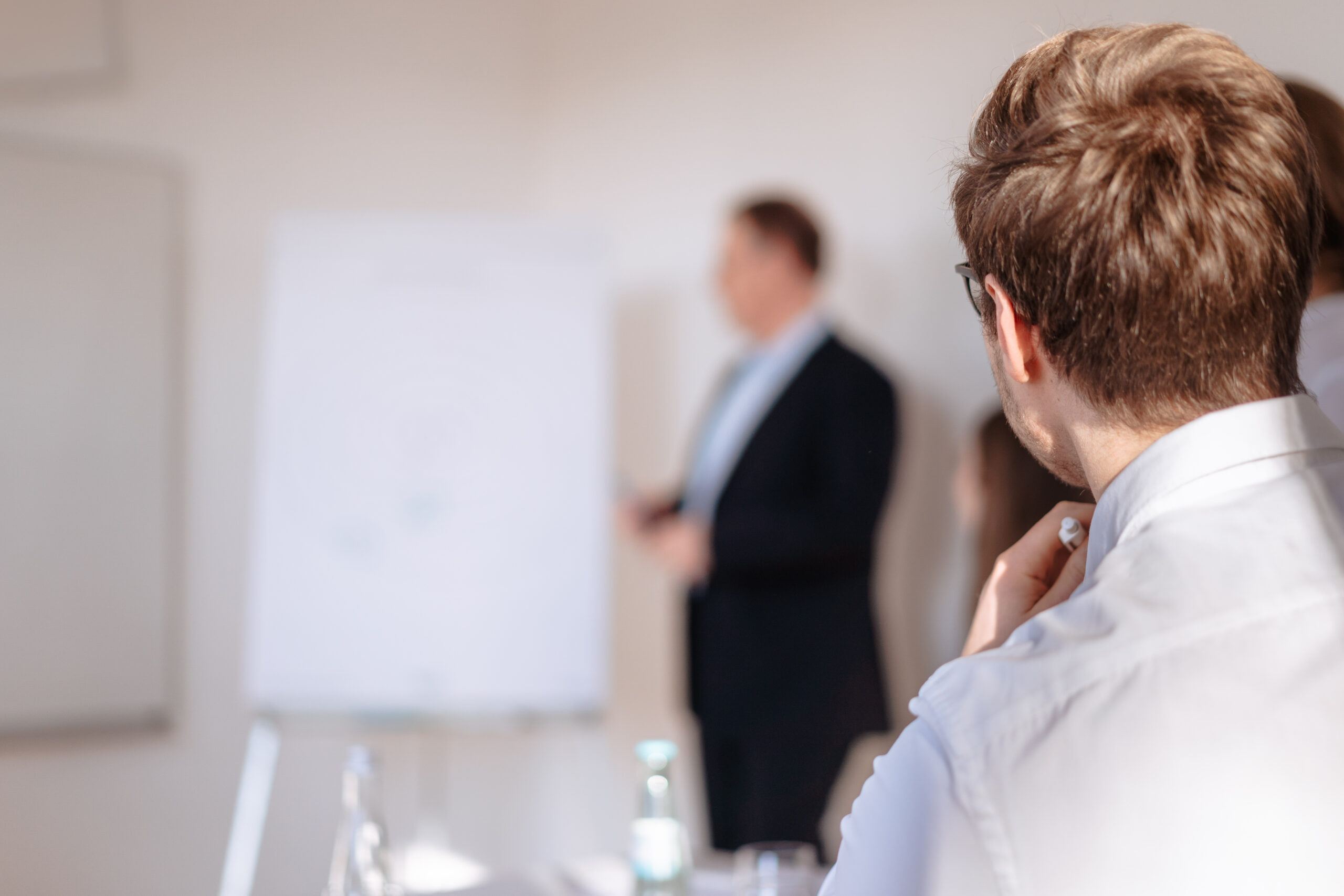 Unser Ansatz Kulturentwicklung Ein Berater steht im Hintergrund vor einem Flipchart, aufmerksam zuhörende Person im Vordergrund, Betrachtung von konkreten Ansatzpunkte für die Entwicklung des Unternehmens, Erarbeiten von Spannungsfeldern