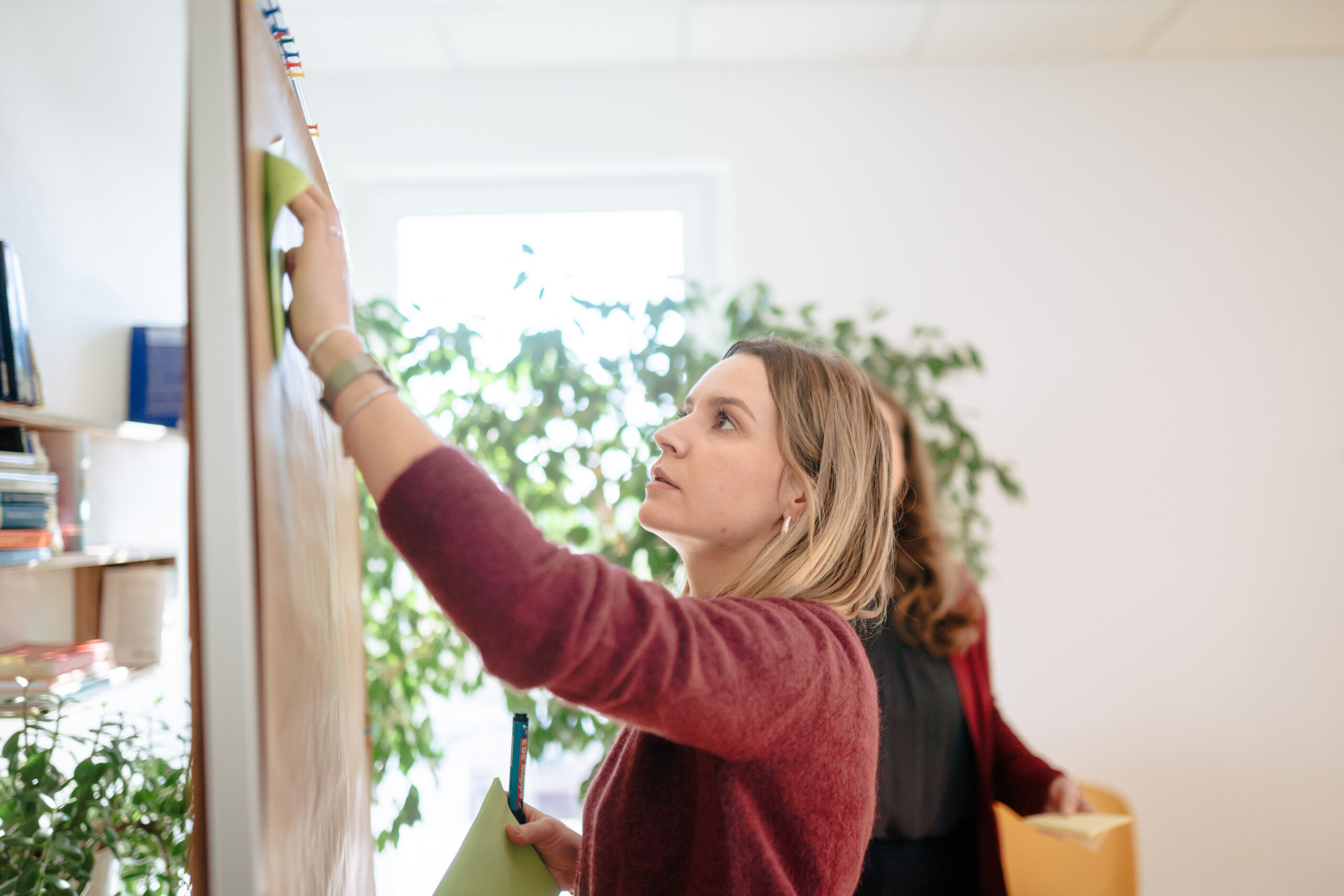Unser Ansatz Teamentwicklung Zwei Personen stehen vor einer Metaplanwand und sortieren Moderationskärtchen, Aufzeigen von unterschiedlichen Perspektiven im Team, Bearbeiten von Konflikten